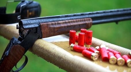 clay shooting gun leaning on bench with red bullets