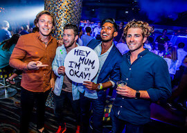 four young men at a bar holding sign and drinking