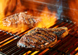 two steaks cooking on bbq with flames