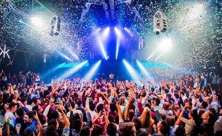 large crowd dancing at nightclub to dj with falling confetti and flashing lights