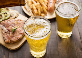 Beer being poured into glass with gourmet steak and french fries on wooden background.